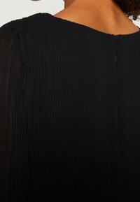 Schwarzes, plissiertes Kleid mit hohem Kragen, das auf der Rückseite eine kleine Schlüssellochöffnung und einen weichen, strukturierten Stoff aufweist.