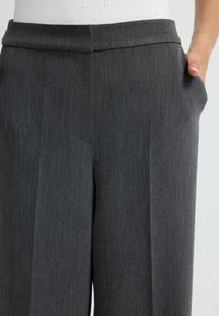 Pantalones grises ajustados con una textura suave, que cuentan con una cinturilla plana y bolsillos laterales. La tela tiene un patrón fino y sutil.