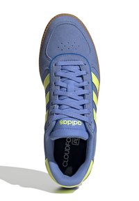 Zapatilla azul de ante y malla con rayas y detalles amarillos. Presenta una lengüeta acolchada y suela de goma. Marca "Cloudfoam" en el interior.