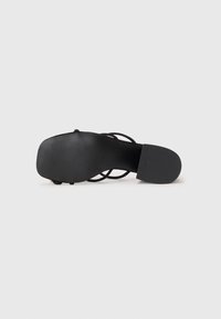 Sandal de tiras negras con suela plana, textura suave y diseño de bandas cruzadas. La suela tiene un patrón acanalado para mayor agarre.