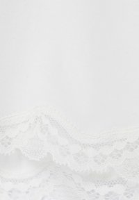 Tessuto bianco con delicata rifinitura in pizzo scallop che presenta motivi floreali e geometrici lungo il bordo.