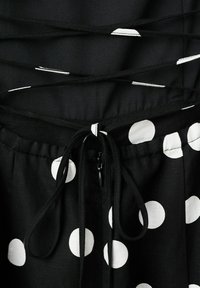 Tela negra con grandes lunares blancos, que presenta un cordón atado y un detalle de cordones negros en una prenda.