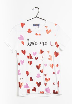 T-shirt blanc à manches courtes avec des cœurs rouges et roses éparpillés et le texte "Love me" en écriture noire sur le devant, suspendu sur un cintre noir.