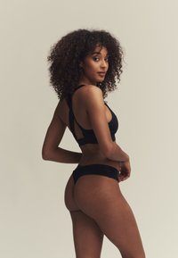 Zwart lingeriesetje bestaande uit een cropped top met een kruisrugontwerp en een naadloze string, met een nadruk op de gladde stofstructuur en minimalistische stijl.
