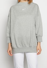 Grå oversized sweatshirt med hög krage och ribbade mudd. Har en liten vit Nike-logotyp på bröstet. Mjuk tygstruktur.