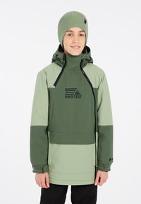 Giacca impermeabile verde con mezza zip, logo nero e cappuccio regolabile. Polsini testurizzati e tonalità di verde a contrasto. Berretto abbinato.