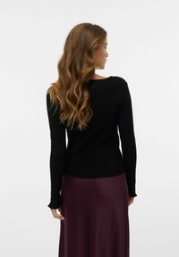 Pull noir à manches longues côtelé avec un col arrondi, associé à une jupe satin prune avec un ourlet froncé.