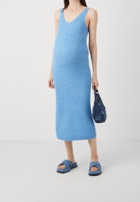 Vestito a maglia azzurro chiaro con scollo a V, forma aderente e lunghezza al ginocchio. Abbinato a sandali blu a scivolo e una borsa blu effetto texture.