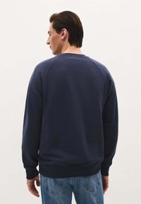 Navyblauwe sweatshirt met een ronde hals, ribgebreide manchetten en zoom. Zacht materiaal, relaxte pasvorm en raglanmouwen, weergegeven vanuit de achterkant.