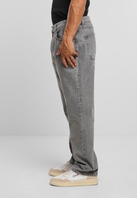 Jeans in denim grigio con vestibilità comoda, dotati di tasche anteriori e posteriori e cuciture visibili; abbinati a sneakers bianche e beige.