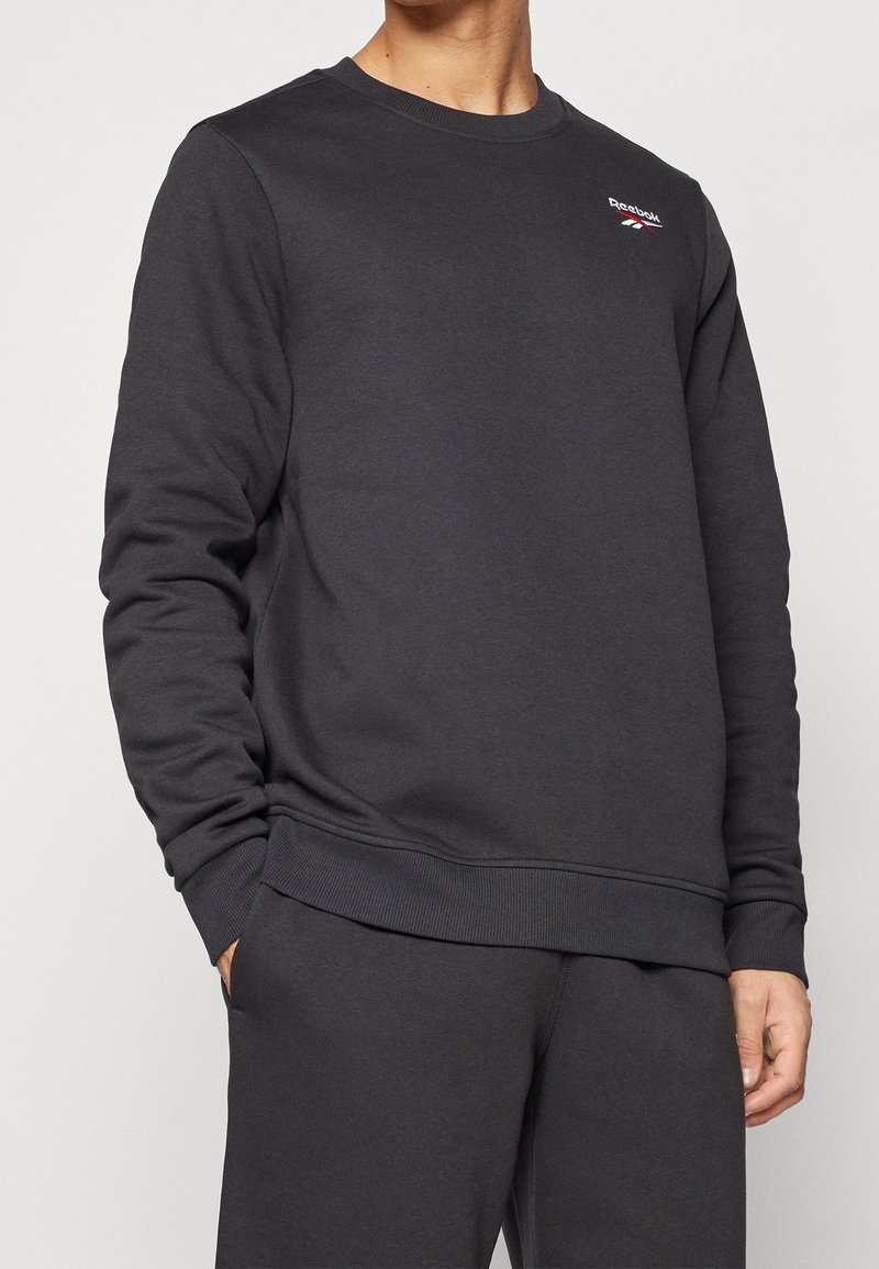 Tmavě šedá mikina s žebrovanými manžetami a lemem. Na hrudi má malé logo. Vyrobena z měkké a strukturované látky.