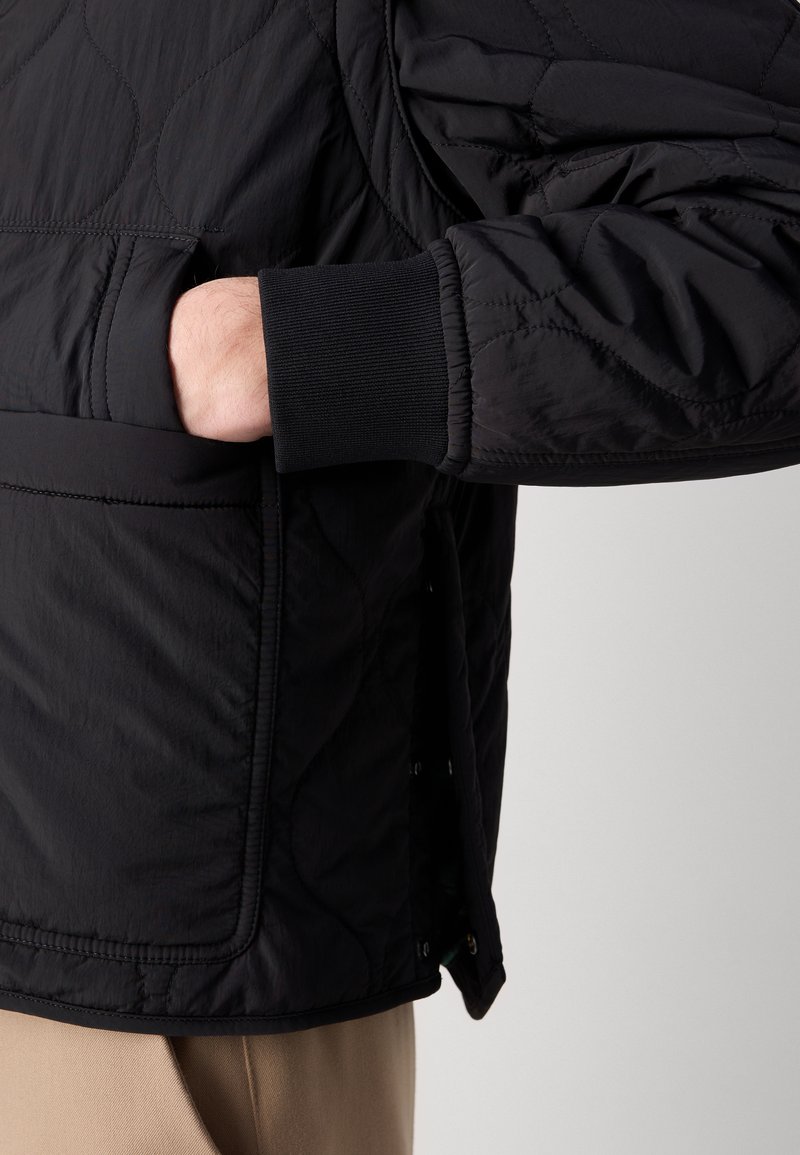Schwarze gesteppte Jacke mit Stehkragen, gerippten Bündchen und Seitentasche. Sie hat eine glatte Textur und eine schlanke Silhouette.