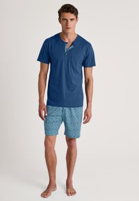 Blauwe katoenen overhemd met korte mouwen, voorzien van een gemusterde halslijn en een borstzak, gecombineerd met gemusterde blauwe shorts in een geometrisch ontwerp.