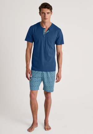 Chemise courte en coton bleu à col à motifs et poche poitrine, associée à un short bleu à motifs en design géométrique.