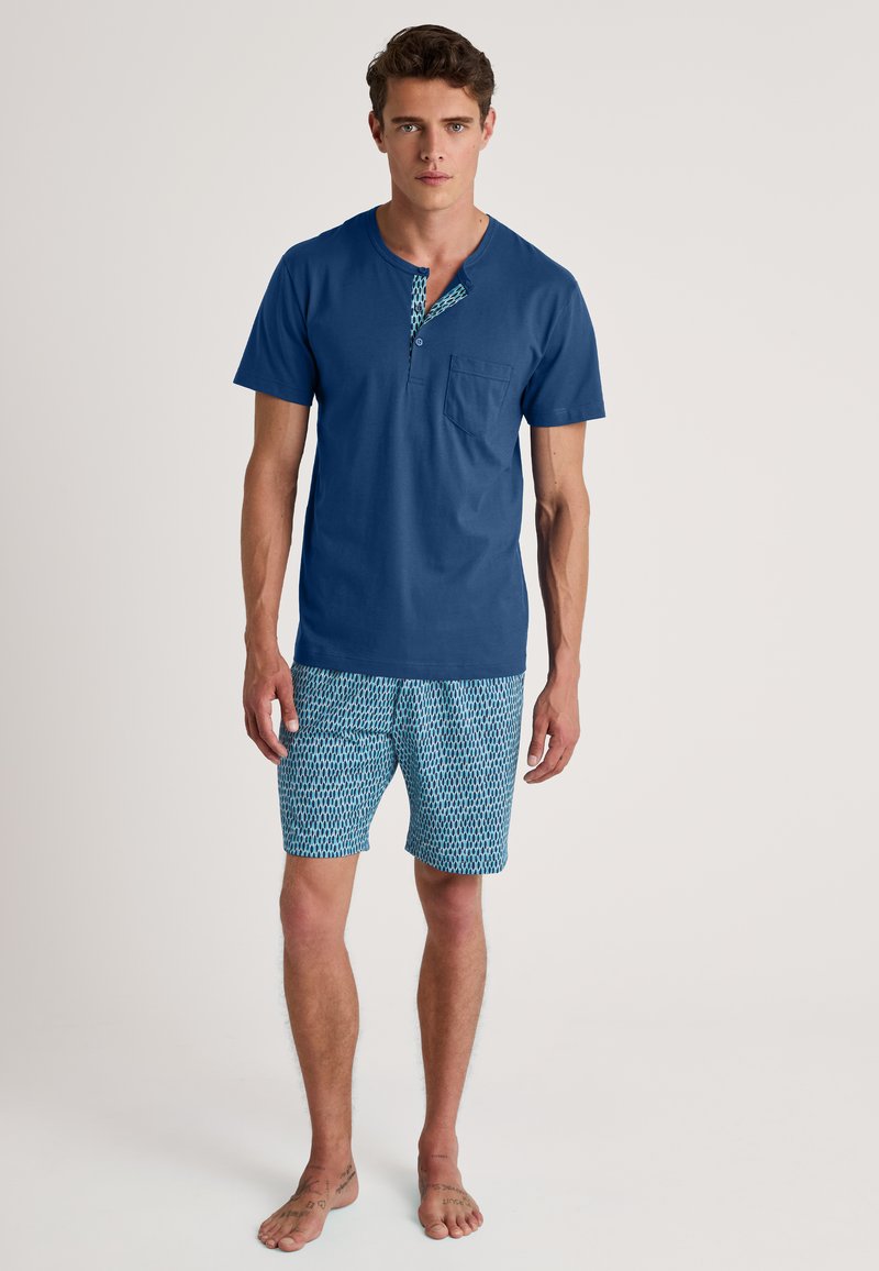 Blauwe katoenen overhemd met korte mouwen, voorzien van een gemusterde halslijn en een borstzak, gecombineerd met gemusterde blauwe shorts in een geometrisch ontwerp.