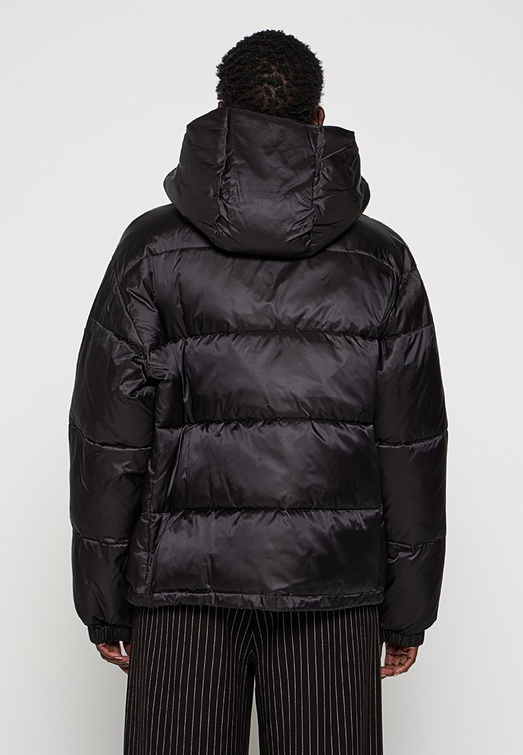 Schwarze Daunenjacke mit Kapuze, ausgestattet mit einem gesteppte Design und elastischen Bündchen. Hergestellt aus glänzendem, glattem Stoff mit einer leicht lockeren Passform.
