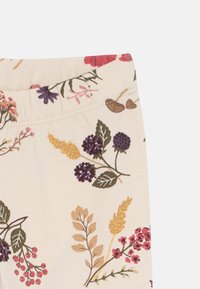 Stoff mit floralem Muster, das verschiedene Blumen und Blätter in rosa, lila und grün auf einem hellbeigen Hintergrund zeigt.