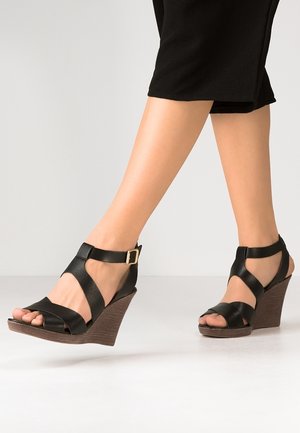 Musta nahka wedge-sandaalit, joissa on hihnadesign, solki ja teksturoitu ruskea wedge-kanta. Avoin varvasmuoto.