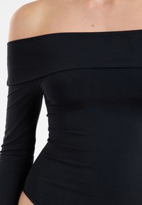 Body noir épaules dénudées en tissu lisse, doté de manches longues et d'une coupe ajustée avec des fronces sur le devant.