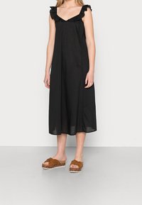 Robe noire sans manches avec bretelles à volants et jupe fluide. Associée à des sandales marron à nœuds, à plateforme à motifs.