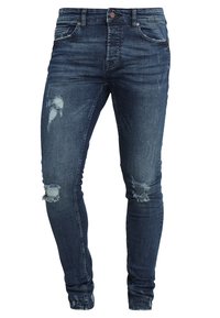 Jeans skinny desgastados de color azul oscuro con rotos en las rodillas, que cuentan con cinco bolsillos, cierre de botón y un diseño ajustado.