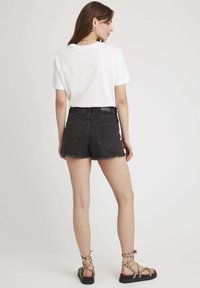 T-shirt en coton blanc à manches courtes, associé à un short en denim noir avec un ourlet effiloché et deux poches arrière, porté avec des sandales à lanières.