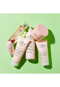 Sex NUXE Body hudvårdsprodukter i olika rosa tuber och en flaska, med grön text och en uppfriskande te-doft, arrangerade på en grön bakgrund.