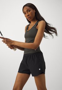 Mørkegrå treningssinglet kombinert med svarte shorts. Shortsen har elastisk midjebånd og en liten logo detalj på siden.