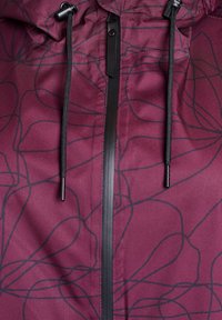 Chaqueta marrón con una textura suave, que presenta un diseño abstracto negro, cremallera frontal y cordones ajustables en la capucha.