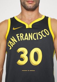 Camiseta de baloncesto negra con acentos amarillos. "SAN FRANCISCO" impreso en amarillo encima del número "30" en un estilo grande y negrita. Logo de Nike presente.