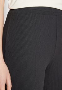 Μαύρο ριγέ κολάν με ψηλή μέση και λεία υφή, σχεδιασμένο για εφαρμογή που αγκαλιάζει το σώμα, με διακριτικές ραφές.