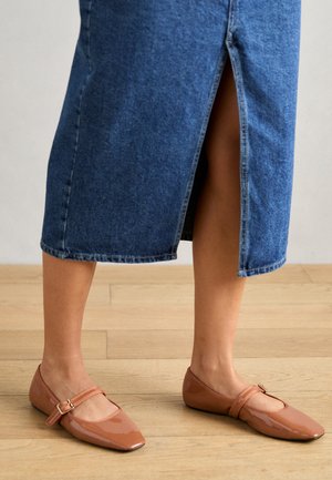 Brown patent leather flats with a square toe and a single strap featuring a buckle. Worn with a mid-length denim skirt.