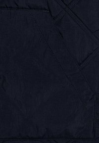 Granatowa pikowana tkanina z wzorem przeszyć ukośnych oraz detalem kieszeni, tworząca teksturowany i strukturalny wygląd.