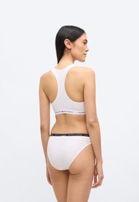 Fehér pamut sportmelltartó versenyzőhát kialakítással, alul fekete logós szalaggal. Hozzáillő fehér hipster alsó hasonló fekete logós derékpánttal.