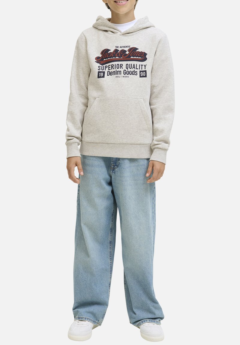 Sweat à capuche gris clair avec une poche à l'avant et un logo imprimé. Associé à un jean large bleu clair et des baskets blanches. Texture lisse.