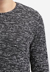 Detailní záběr osoby v černobíle texturovaném pleteném svetru s kulatým výstřihem a dlouhými rukávy.
