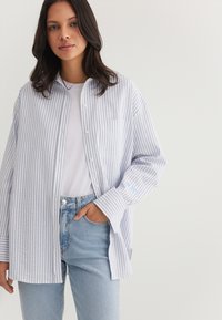 Light blue and white striped button-up shirt with long sleeves, featuring a single chest pocket and embroidered detail on the sleeve.