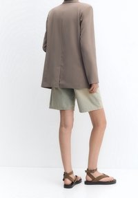 Blazer structuré marron, short en denim vert délavé, et sandales marron à multiples brides avec une semelle texturée.