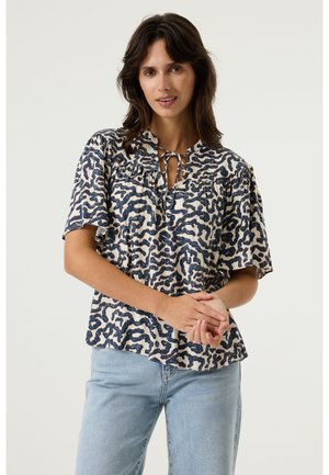Blouse à manches courtes, coupe ample, en tissu léger ; présente une base crème avec des motifs abstraits bleu marine et un col noué.