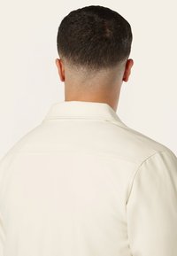 Lichtcrème kleurige shirt met een kraag, gladde textuur, zichtbare stiksels langs de schoudernaad, en een schoon, minimalistisch ontwerp.
