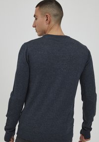 Maglione lavorato a maglia blu scuro con colletto rotondo, maniche lunghe e polsini a coste. Il tessuto presenta una sottile trama con una finitura liscia.