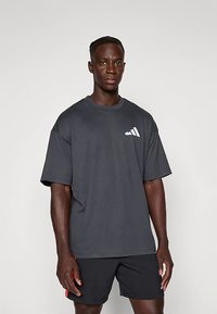 Dark gray oversized t-shirt in a soft fabric, featuring short sleeves and a white Adidas logo on the chest. Simple, relaxed fit design.