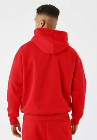 Felpa rossa con cappuccio e pantaloni abbinati. Realizzata in morbido tessuto, presenta polsini e orlo a costine, con una vestibilità comoda e dettagli minimi.