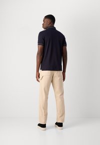 Marineblauw polo shirt met korte mouwen en een contrasterende kraag, gecombineerd met beige cargobroeken met zijzakken en zwarte sneakers.