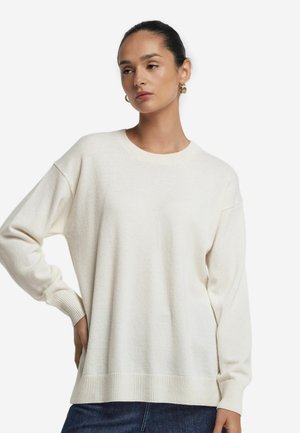 Krämfärgad oversized tröja gjord av mjukt tyg, med rundad halsringning, ribbade ärmslut och en avslappnad passform.