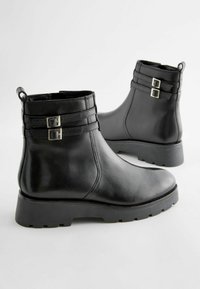 Bottines en cuir noir avec une finition lisse, dotées de deux sangles décoratives et de boucles en métal argenté, ainsi que d'une semelle en caoutchouc robuste.