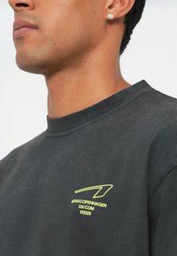 Zwarte katoenen sweatshirt met een ronde hals. Heeft een groen logo en tekst gedrukt op de linkerborst. Zacht, lichtjes gestructureerd materiaal.