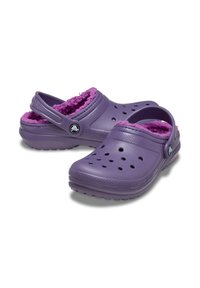 Sabots violets avec une doublure en peluche rose, dotés de trous de ventilation, d'une bride arrière et d'un accent de logo contrastant sur le côté.