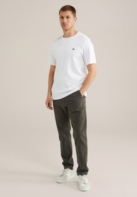 Witte t-shirt met korte mouwen en een klein logo op de borst, gecombineerd met donkergroene broek en witte sneakers. Eenvoudig ontwerp en getailleerde stijl.