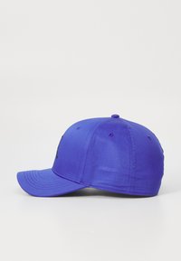 Lila keps med böjd skärm, strukturerad design och svart logotyp på framsidan. Tillverkad av slätt tyg med ventilationshål.